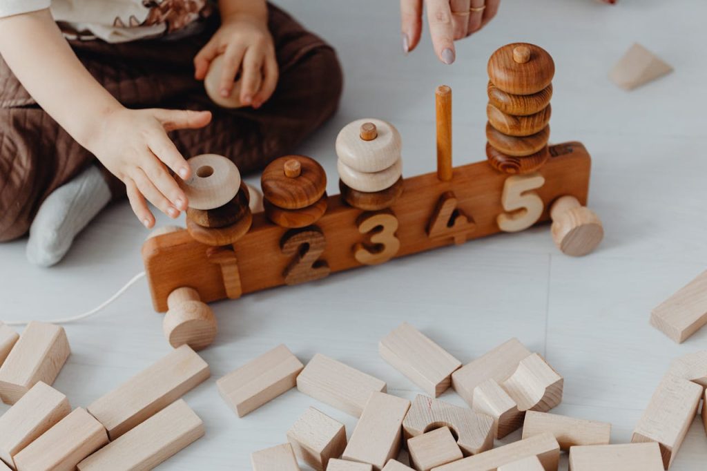 child-playing-with-toy-blocks-and-numbers-7269676 Child engaging with wooden blocks and train toy for learning numbers interactively.