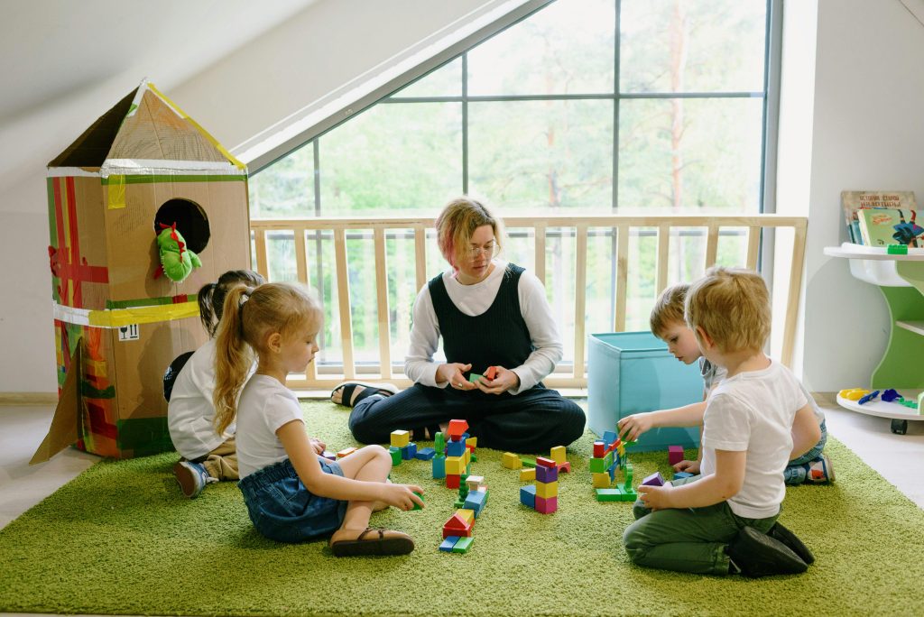 pexels-photo-8535183-8535183 Children enjoying playtime with blocks and cardboard house in a cozy classroom.