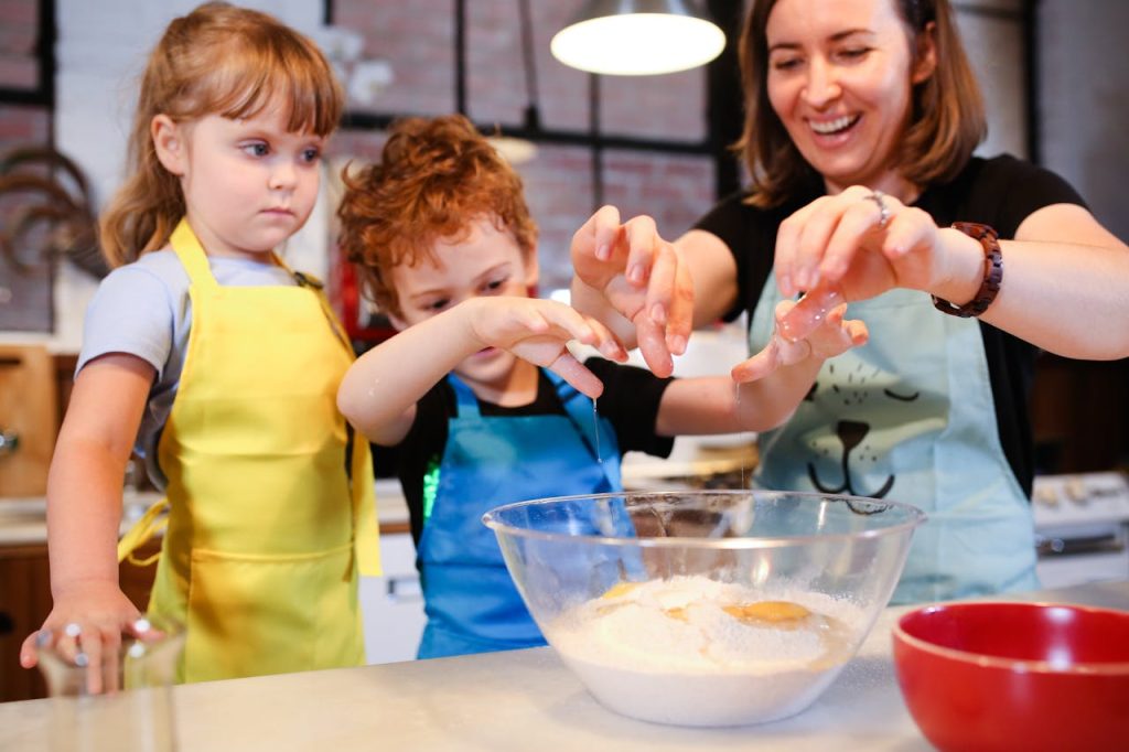 woman-in-yellow-shirt-holding-girl-in-blue-shirt-5593699 Children and a woman joyfully baking cookies together, learning cooking skills.